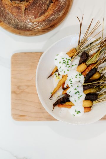 bowl of carrots with yogurt sauce sitting on a cutting board and a loaf of sourdough bread in the background