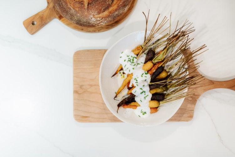 bowl of carrots with yogurt sauce sitting on a cutting board and a loaf of sourdough bread in the background