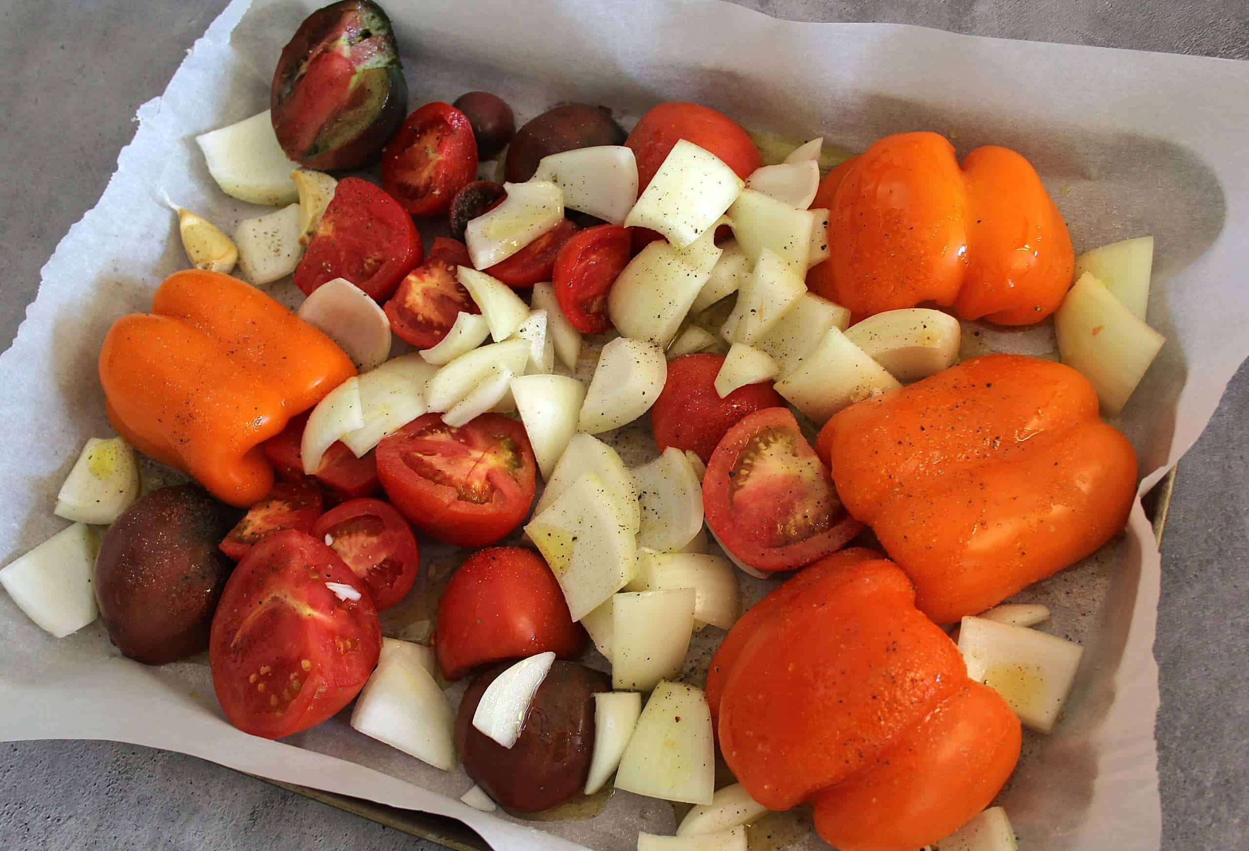 A baking sheet with bell peppers, onions, tomatoes and garlic