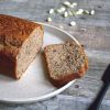 a loaf and a slice of banana bread on a plate with a knife and cardamom pods in the background