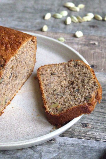 a loaf and a slice of banana bread on a plate with a knife and cardamom pods in the background