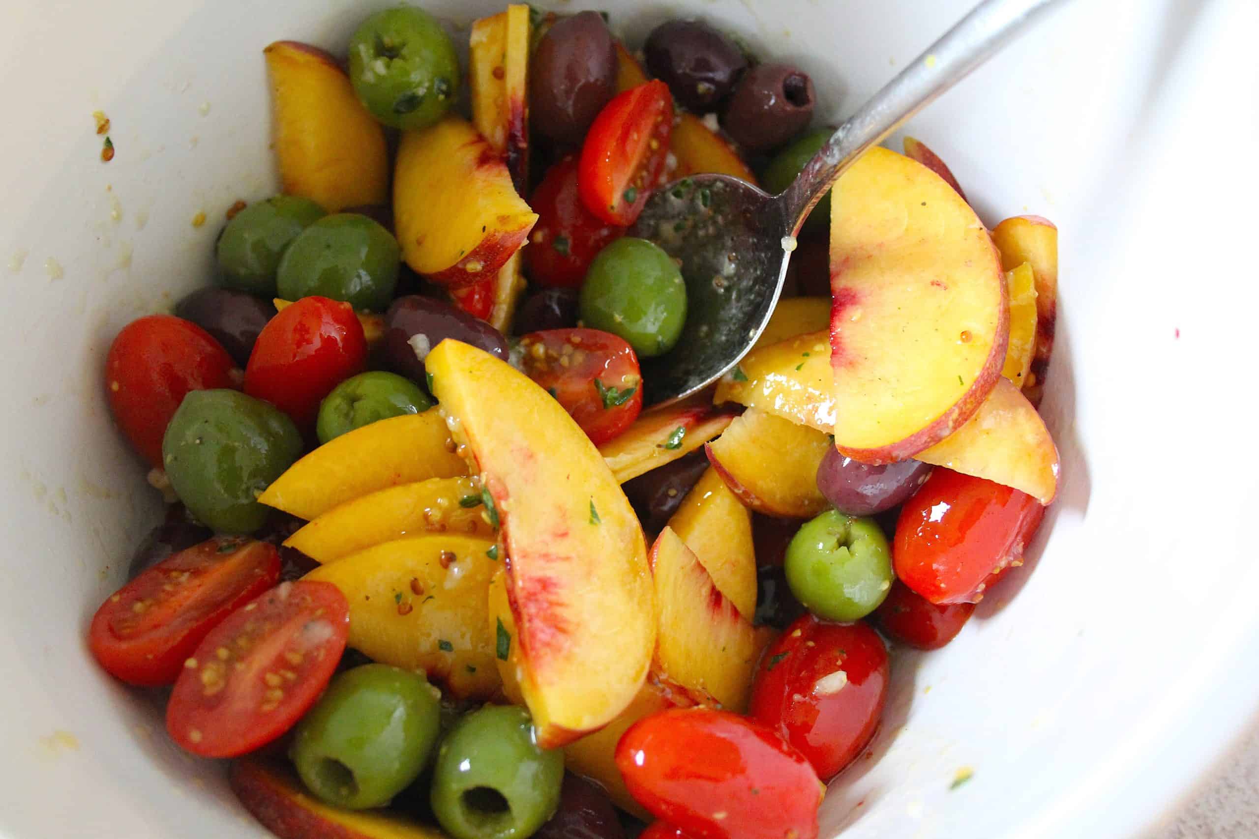 peaches, tomatoes and olives tossed in dressing in a bowl