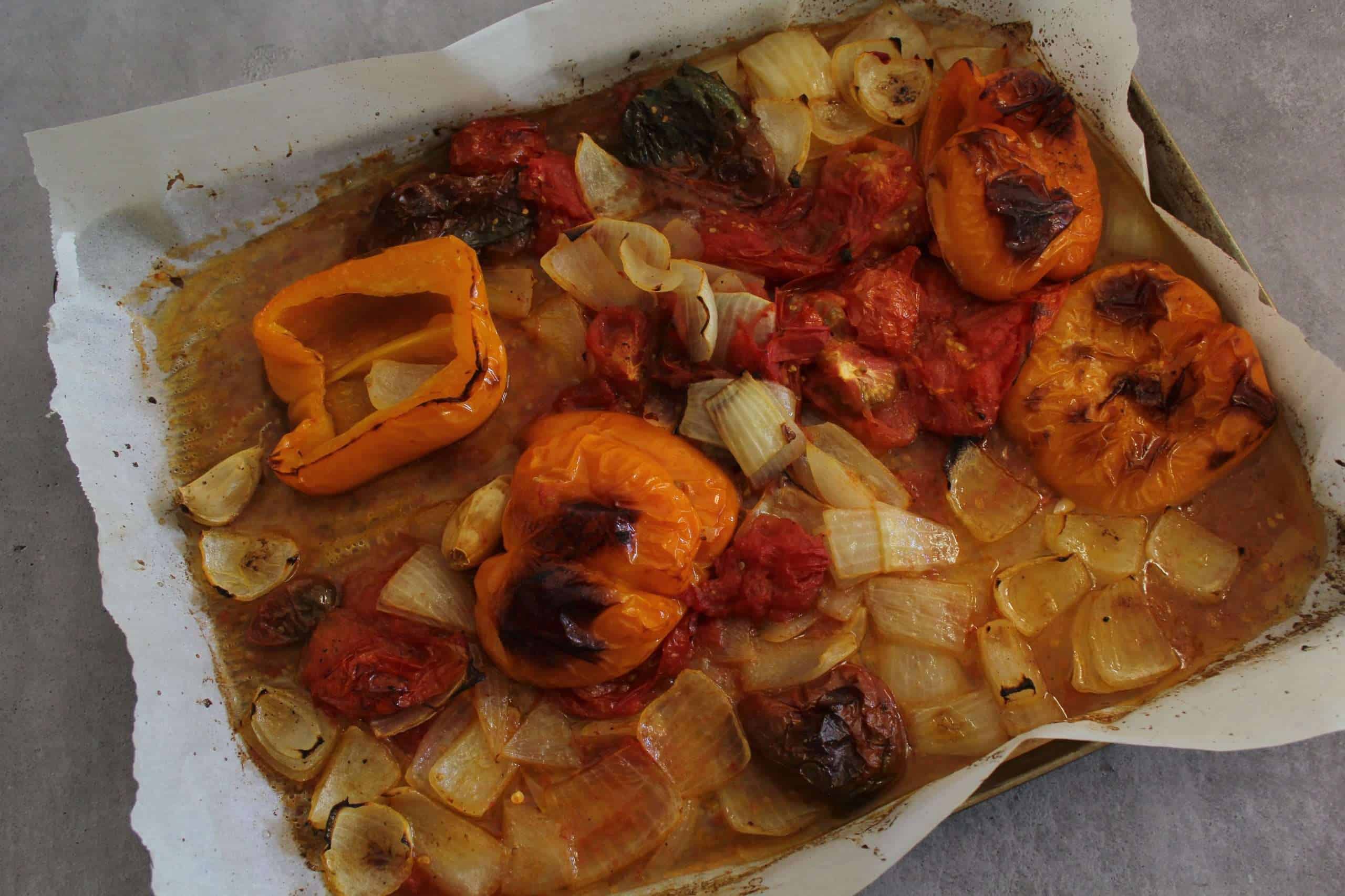 A baking sheet with roasted bell peppers, tomatoes, onions and garlic
