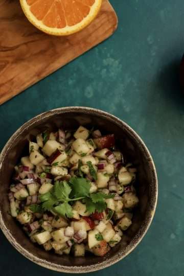 a bowl of pear salsa along with a whole pear and a cutting board holding half an orange, a jalapeno pepper and diced red onions