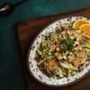 A small white and blue platter with wild rice and salmon bowl with fall veggies topped with pear salsa is placed on a wooden board - a small bowl of pear salsa can be partially seen, along with a black spoon
