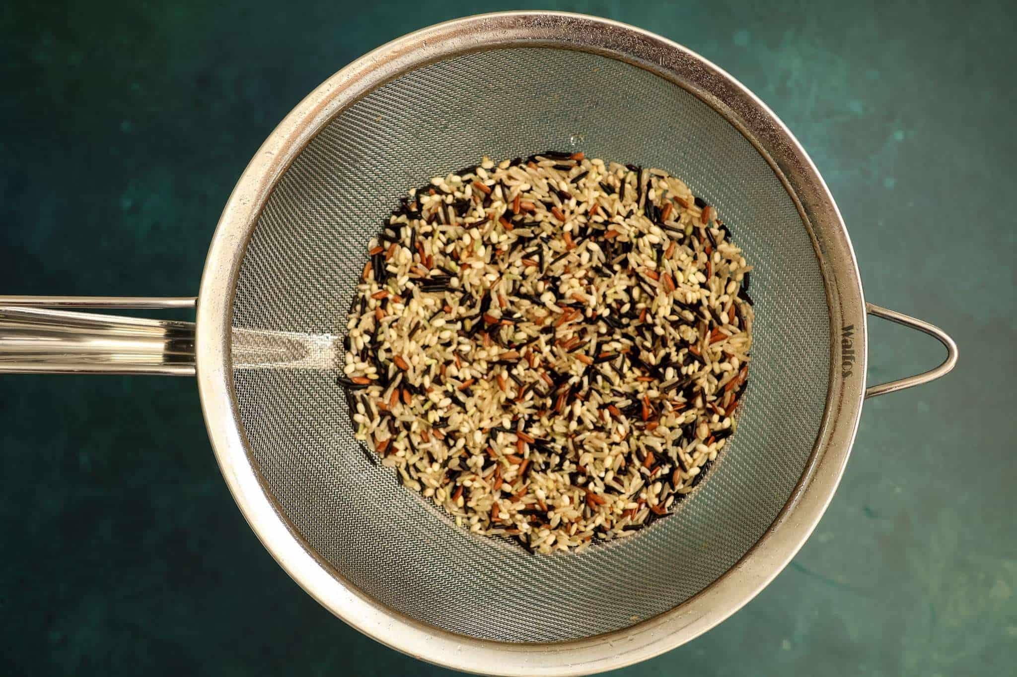 A sieve containing wild rice placed over a small pot