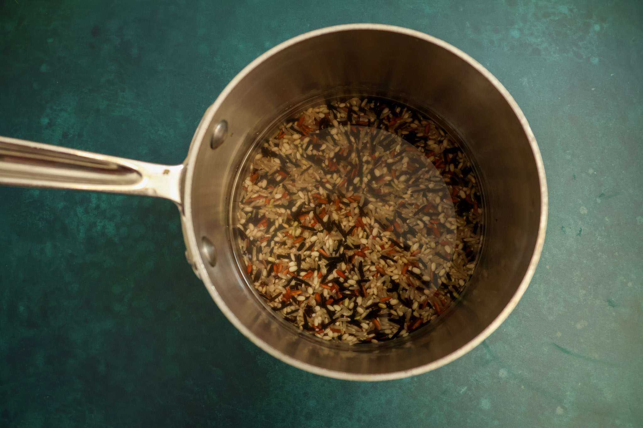 a small pot with wild rice, water, and salt ready to be cooked on a dark turquoise background