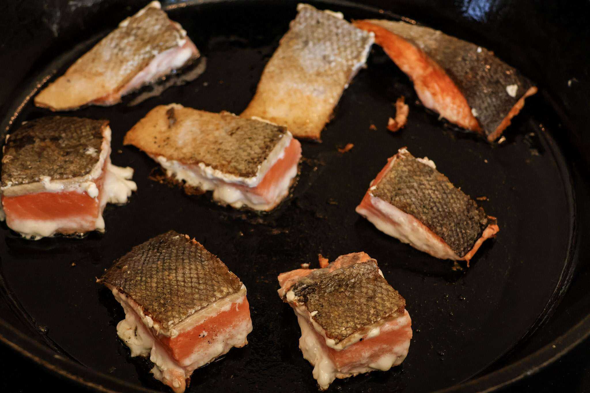 8 chunks of salmon sauteing skin-side up in a cast iron pan