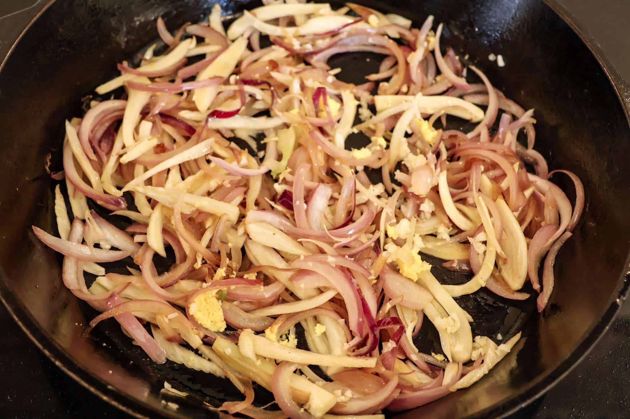sliced onions, fennel, garlic and ginger sauteing in a cast iron pan