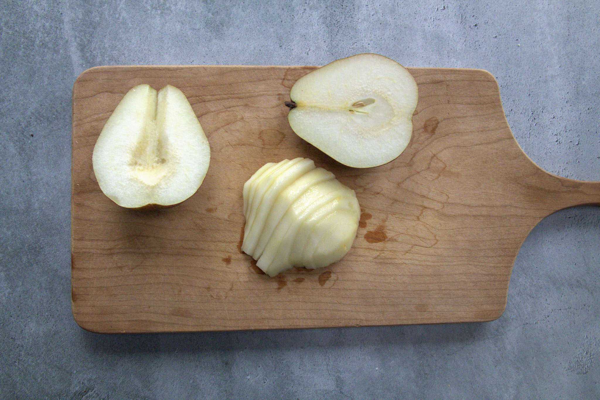 Three pear halves are on a cutting board - one is fully intact with the core, one is cored and the third is cored and sliced