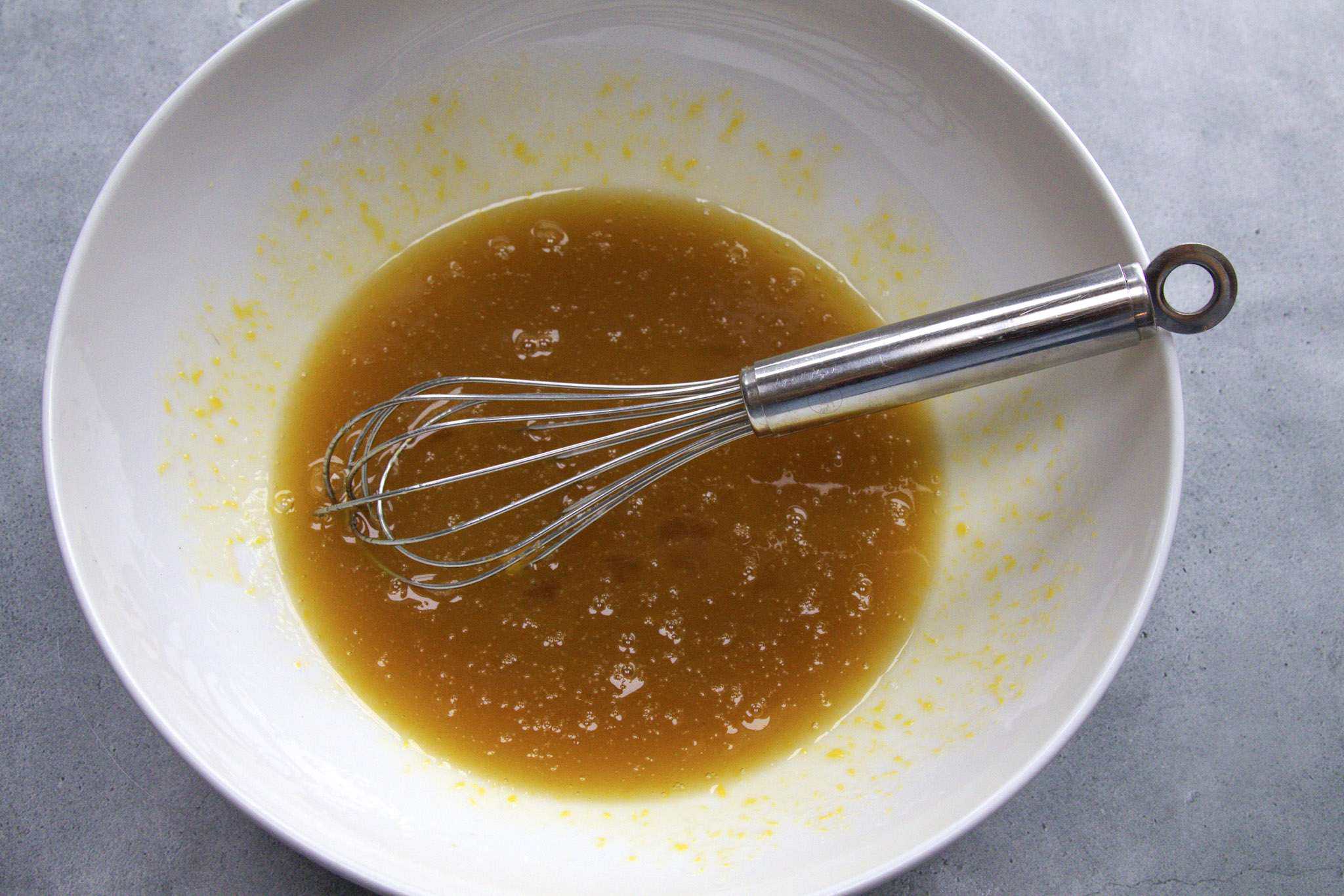 The blended wet ingredients for pear almond coffee cake (gluten-free) are in a white bowl with a whisk resting in it
