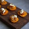 a wooden board with sliced sweet potatoes that are topped with apple chutney, goat cheese and thyme leaves