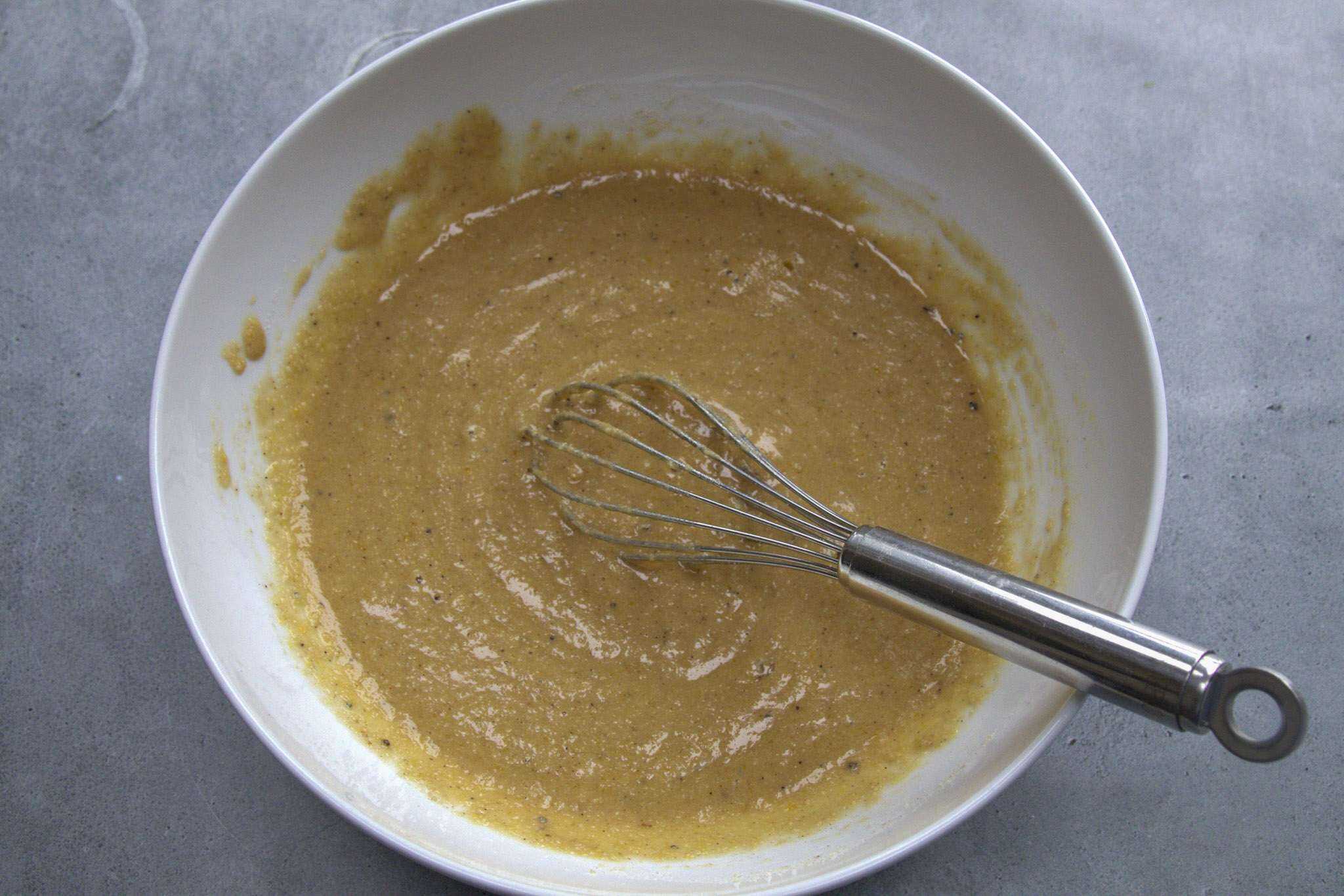 The prepared batter for pear almond coffee cake (gluten-free) is in a white bowl with a whisk resting inside of the bowl