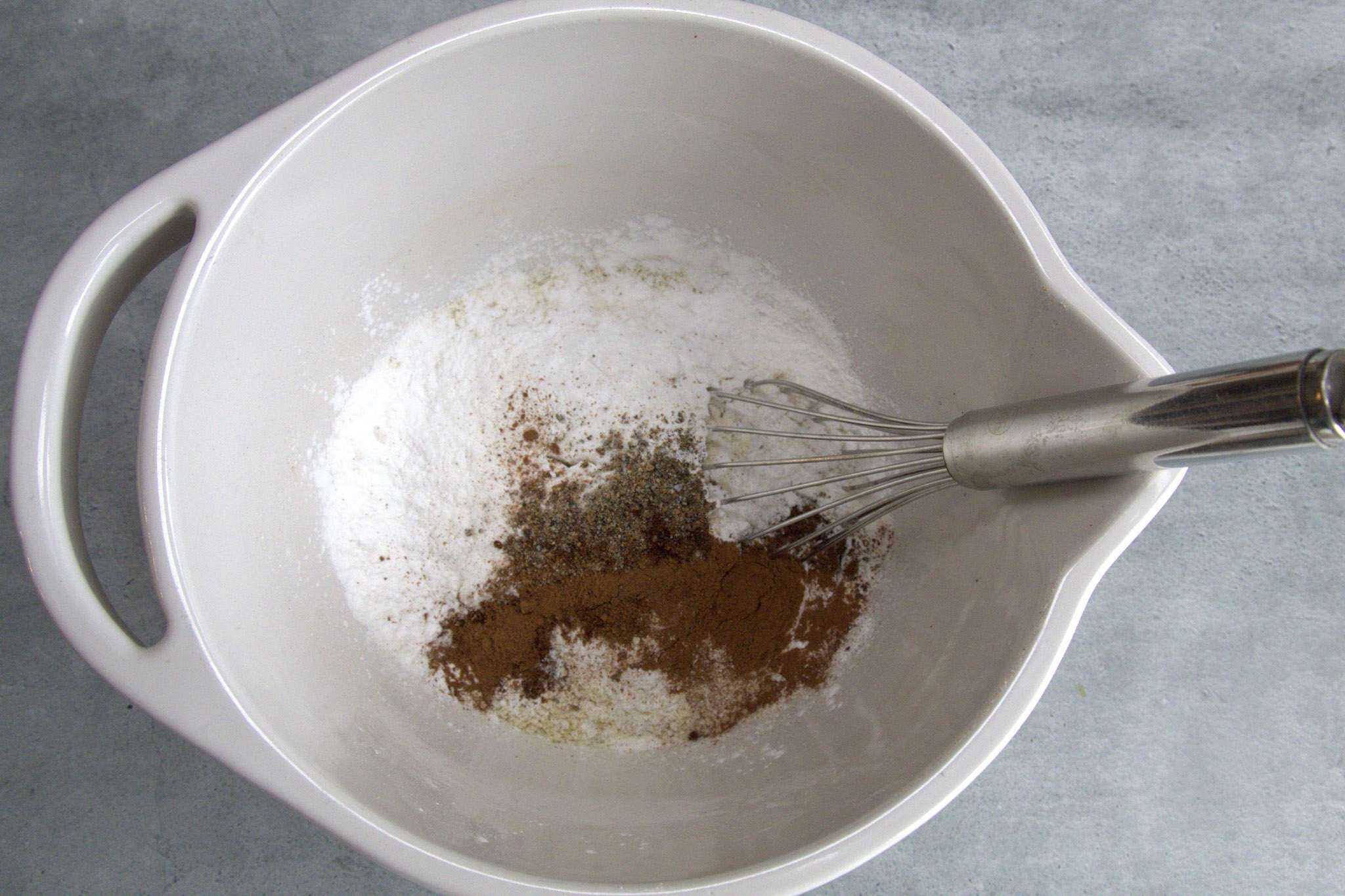 the dry ingredients for pear almond coffee cake (gluten-free) are in a white bowl with a whisk resting in it