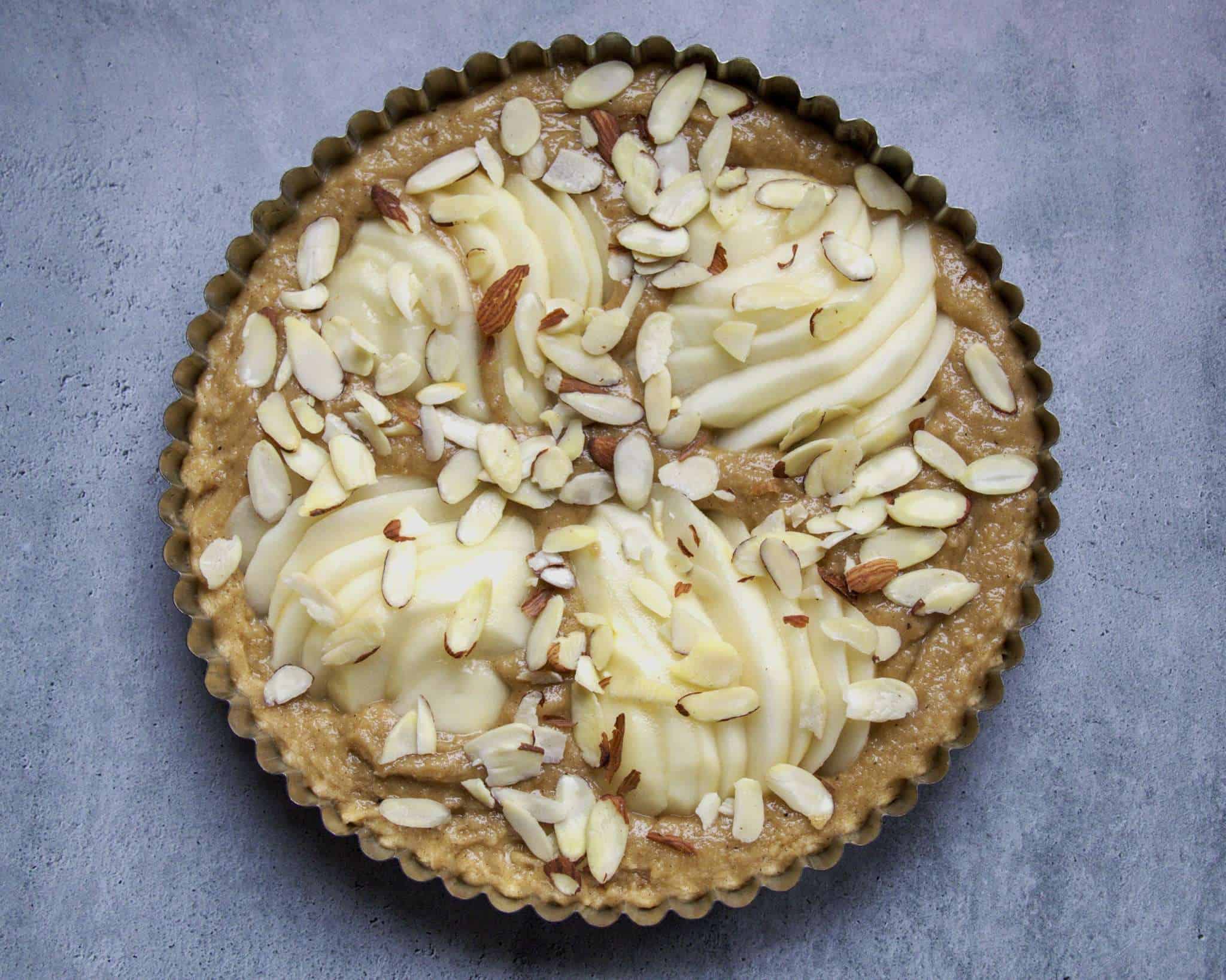 an unbaked pear almond coffee cake in a tart pan ready to bake