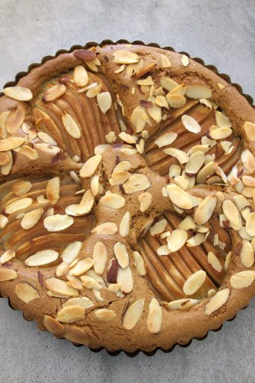 Pear and almond coffee cake with a serving utensil and whole cloves in the background