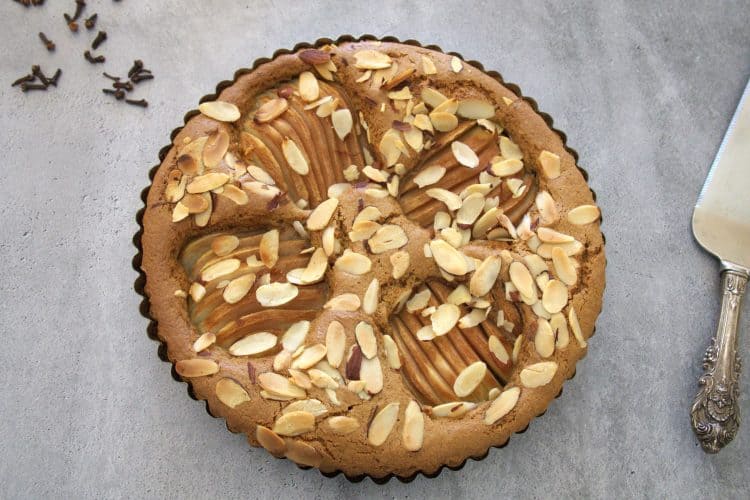 Pear and almond coffee cake with a serving utensil and whole cloves in the background