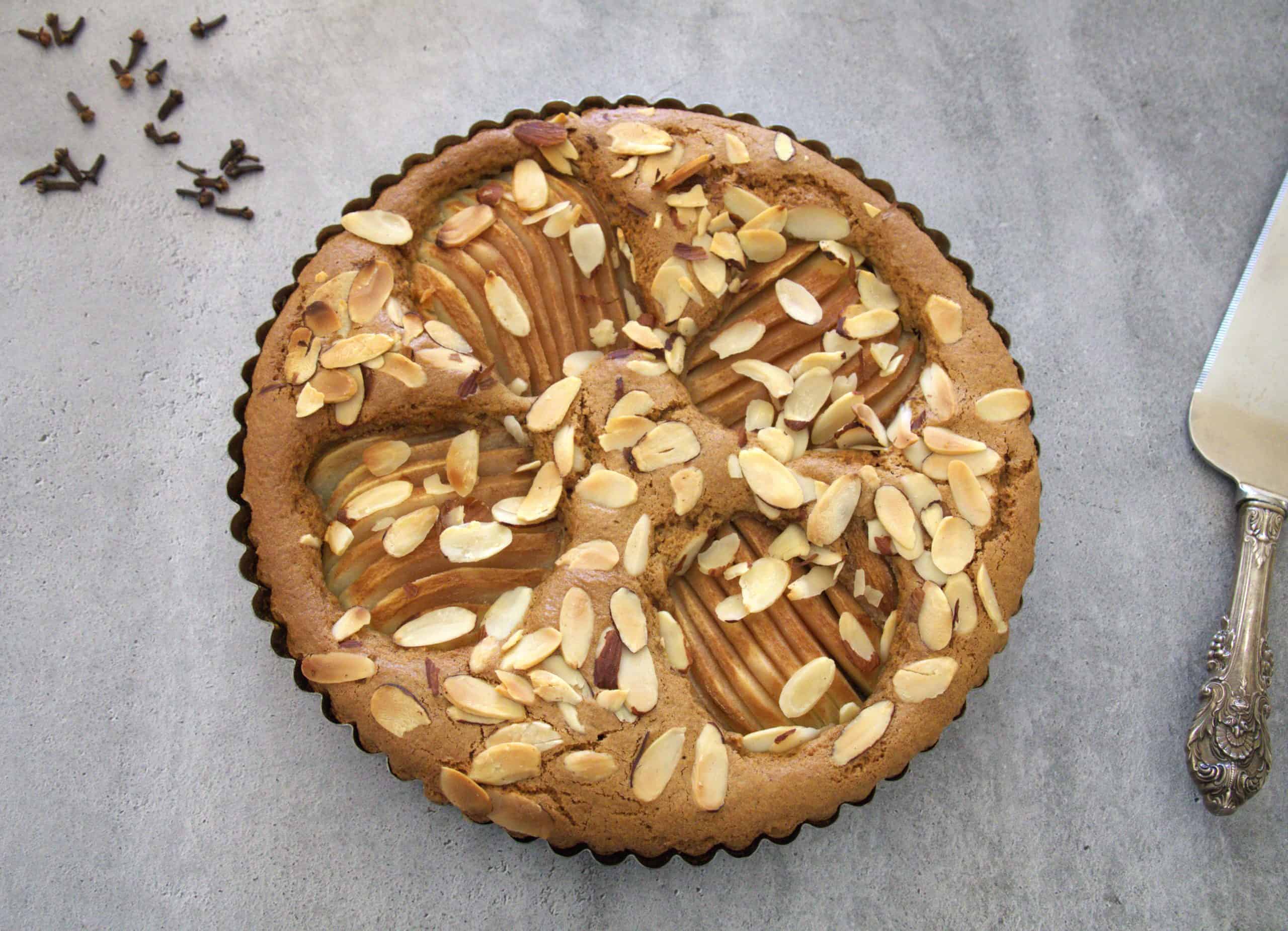 Pear and almond coffee cake with a serving utensil and whole cloves in the background
