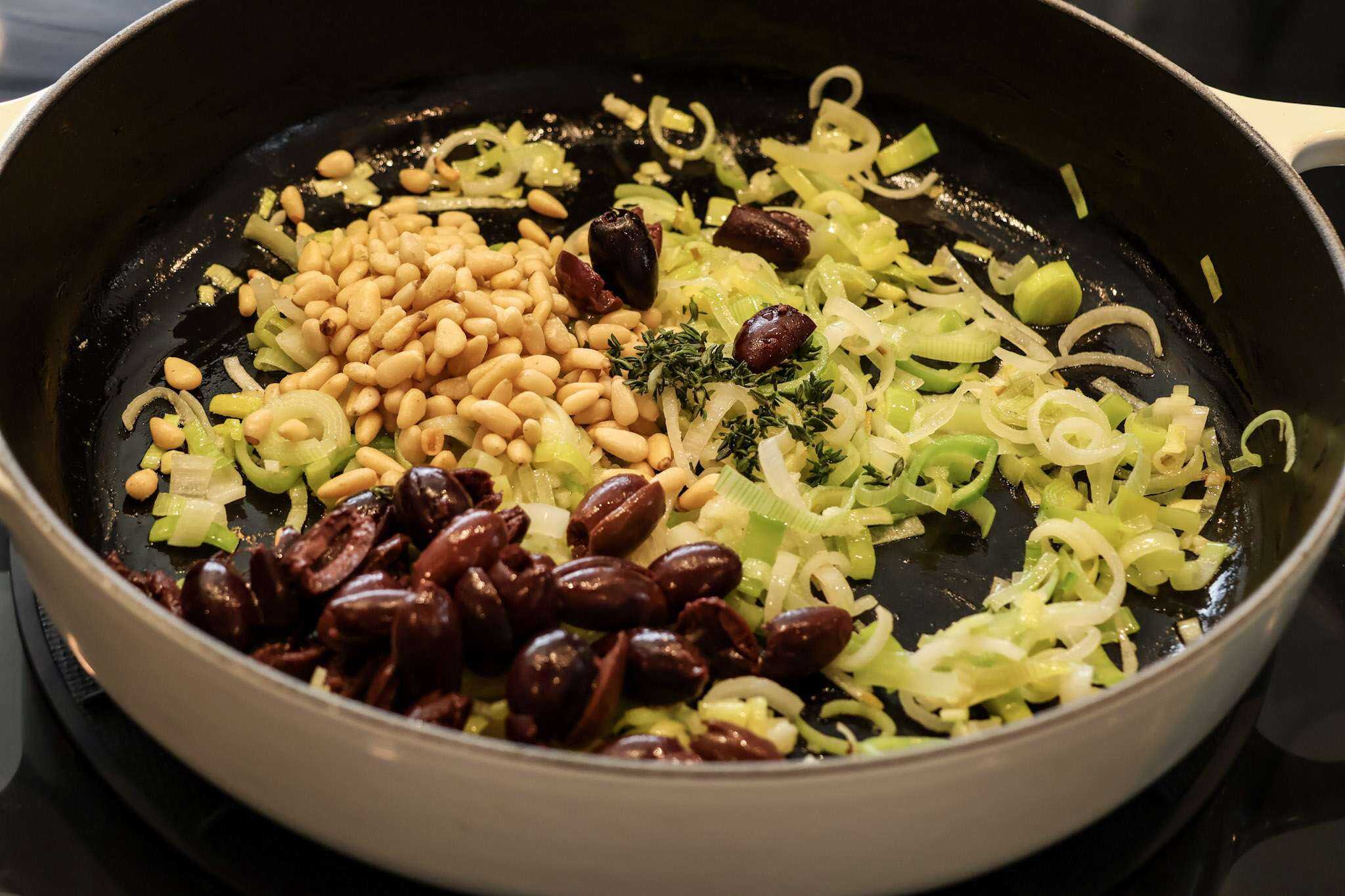 thinly sliced leeks, olive, and pine nuts sauteing in a pan