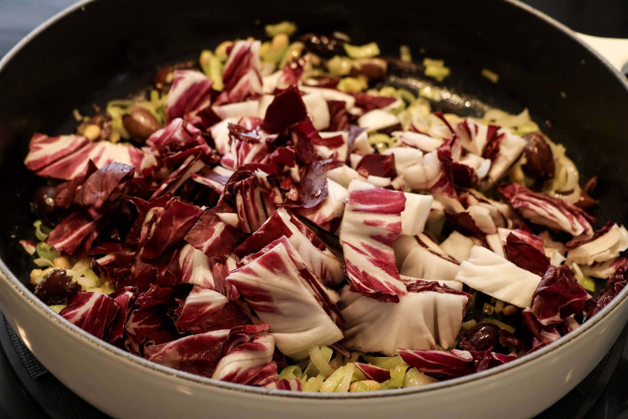 thinly sliced leeks, olives, pine nuts, and radicchio sauteing in a pan