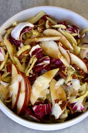 a bowl with salad made up of radicchio, sliced pears, fennel, pecans, shaved pecorino romano cheese and dressing
