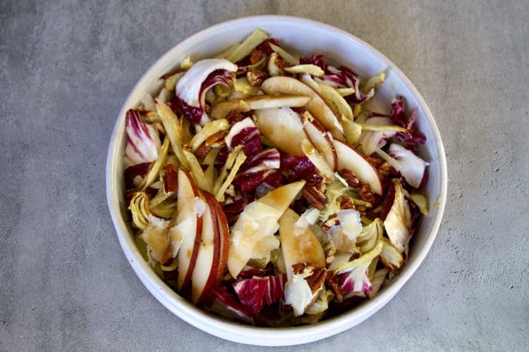a bowl with salad made up of radicchio, sliced pears, fennel, pecans, shaved pecorino romano cheese and dressing