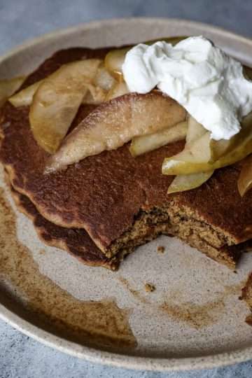 plate of gingerbread pancakes topped with pears and yogurt, a fork resting on the side with a piece of pancake on it and a napkin on the side
