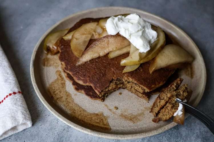 plate of gingerbread pancakes topped with pears and yogurt, a fork resting on the side with a piece of pancake on it and a napkin on the side