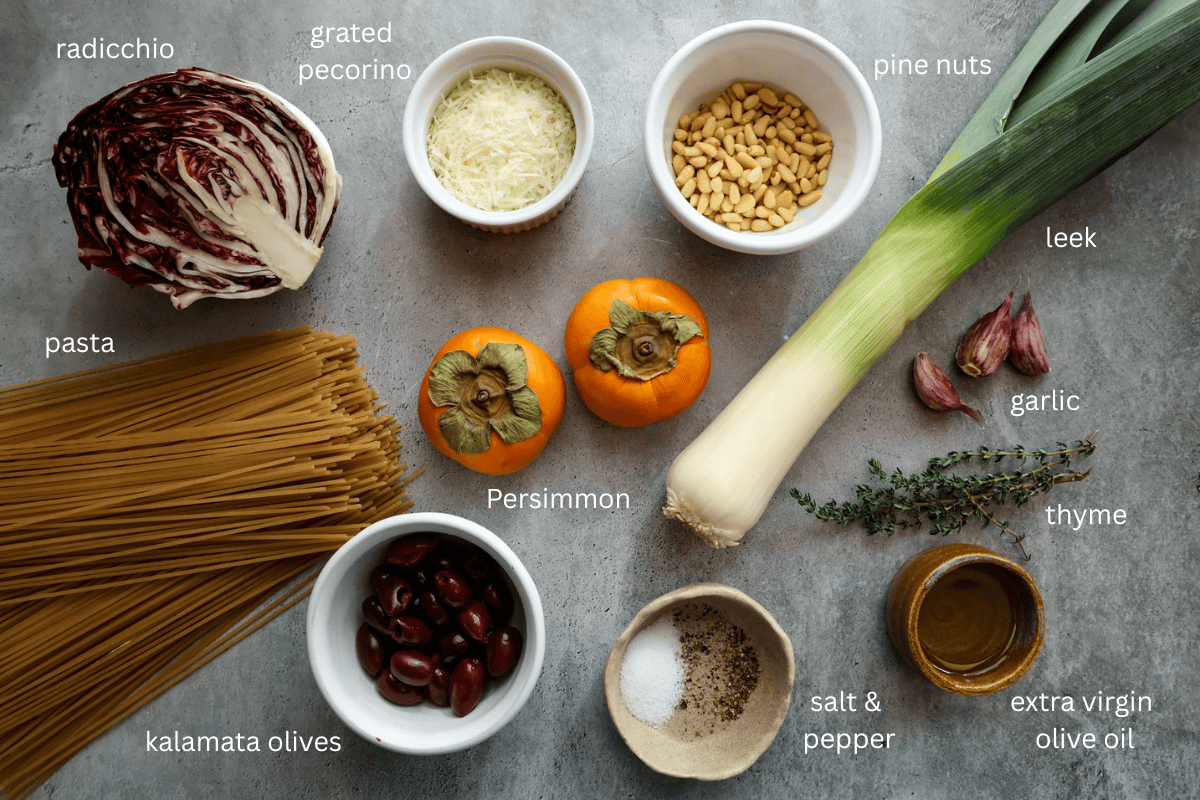 All, labeled, ingredients for roasted persimmon and radicchio pasta on a grey concrete style surface