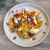 plate with roasted squash, shallots, pears, goat cheese, pomegranate seeds and a drizzle of balsamic reduction