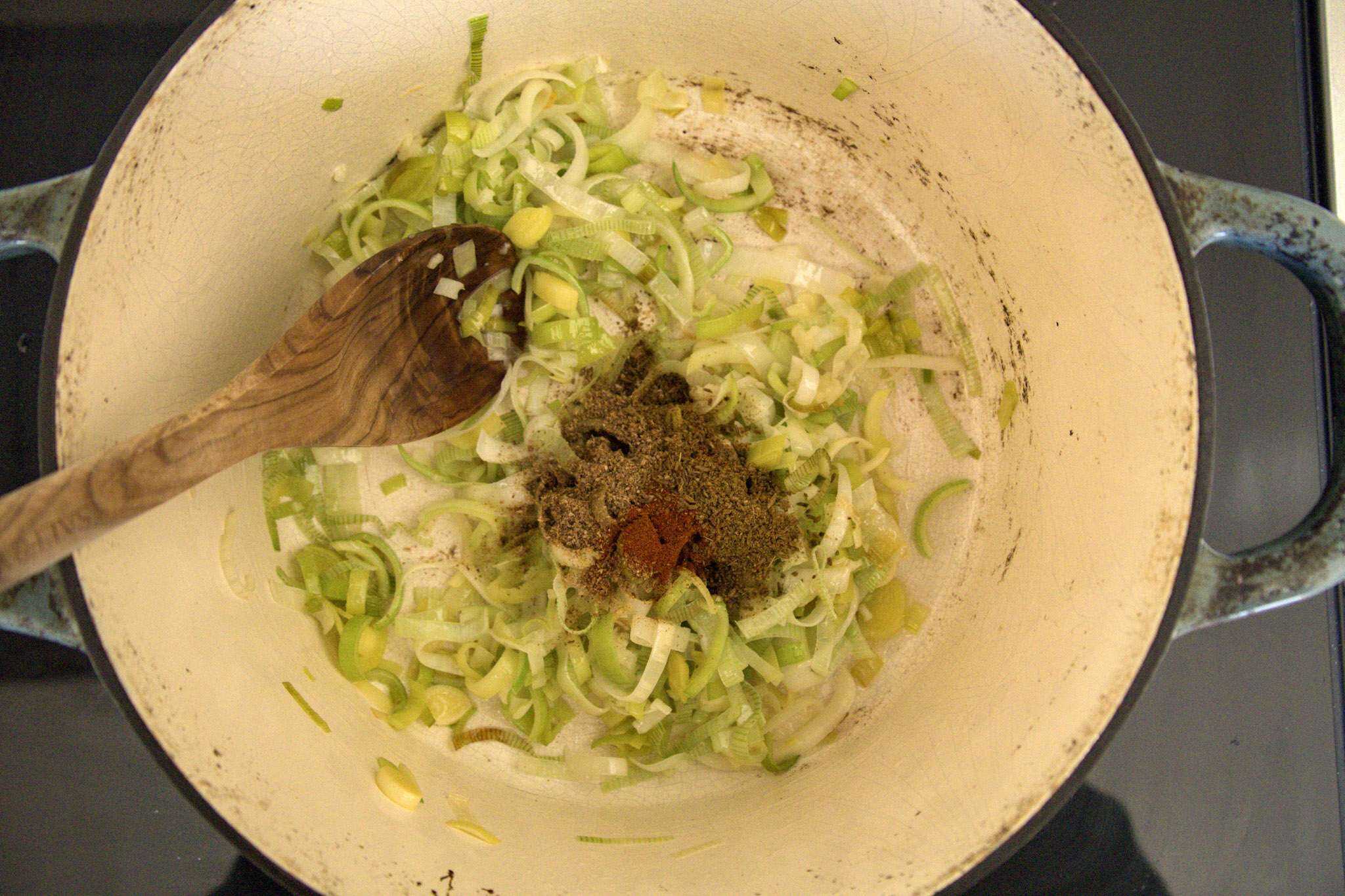 thinly sliced leeks, minced garlic, sauteing in a pot along with spices that were just added - a wooden spoon can be seen