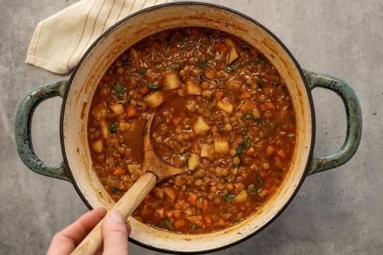 A Dutch oven with celeriac and lentil soup and a wooden ladle resting in it