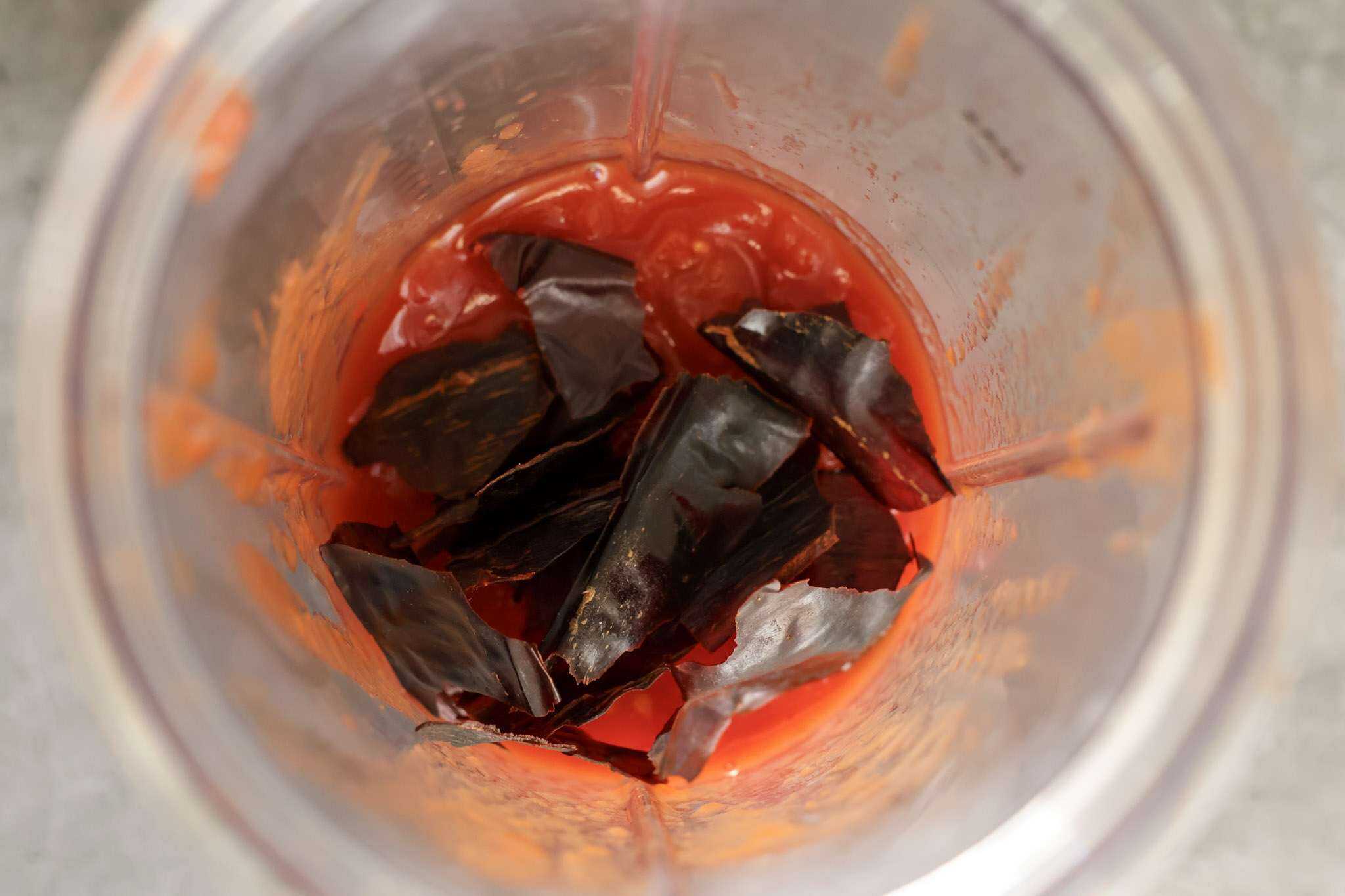 Diced tomatoes and a seeded and torn guajillo chili are in a small blender container
