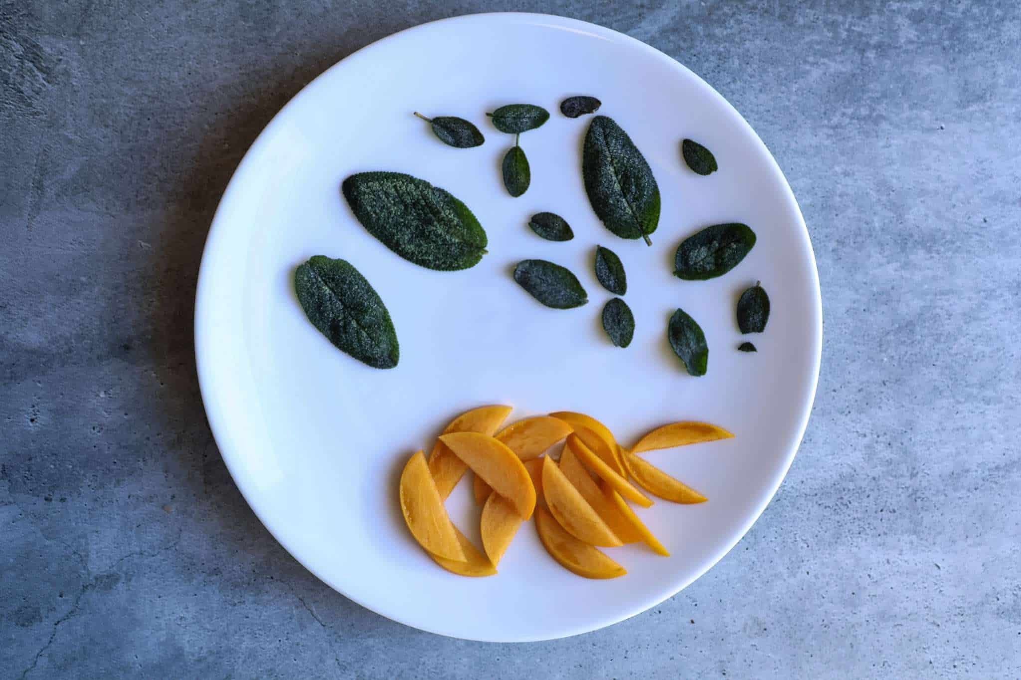 fried sage leaves and sliced persimmons on a white plate
