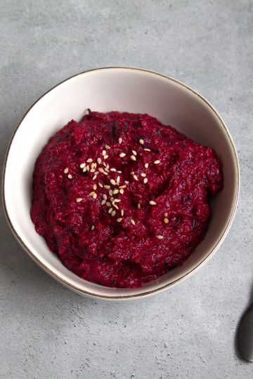 bowl with beet pesto and sesame seeds sprinkled on top and a spoon resting next to the bowl