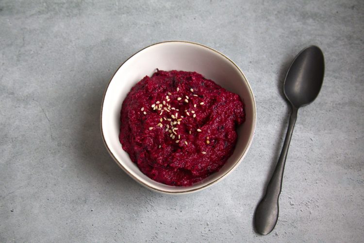 bowl with beet pesto and sesame seeds sprinkled on top and a spoon resting next to the bowl