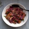 Bowl with beet salad and a spoon resting in it and napkin in the background