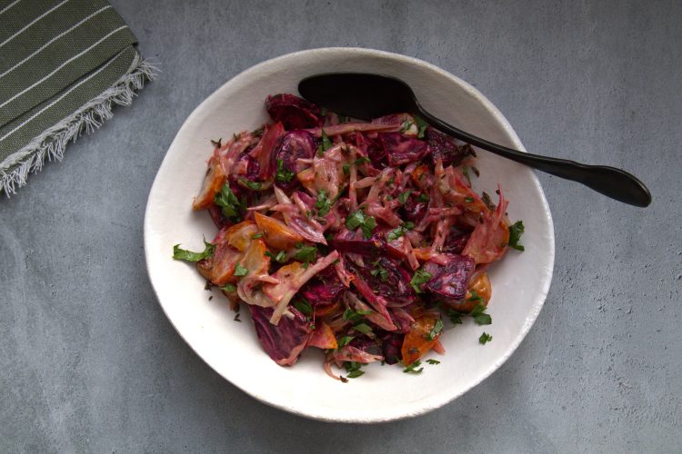 Bowl with beet salad and a spoon resting in it and napkin in the background