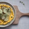 cutting board with a plate on it that is holding a bed of carrot hummus topped with roasted fennel, chopped hazelnuts and thyme