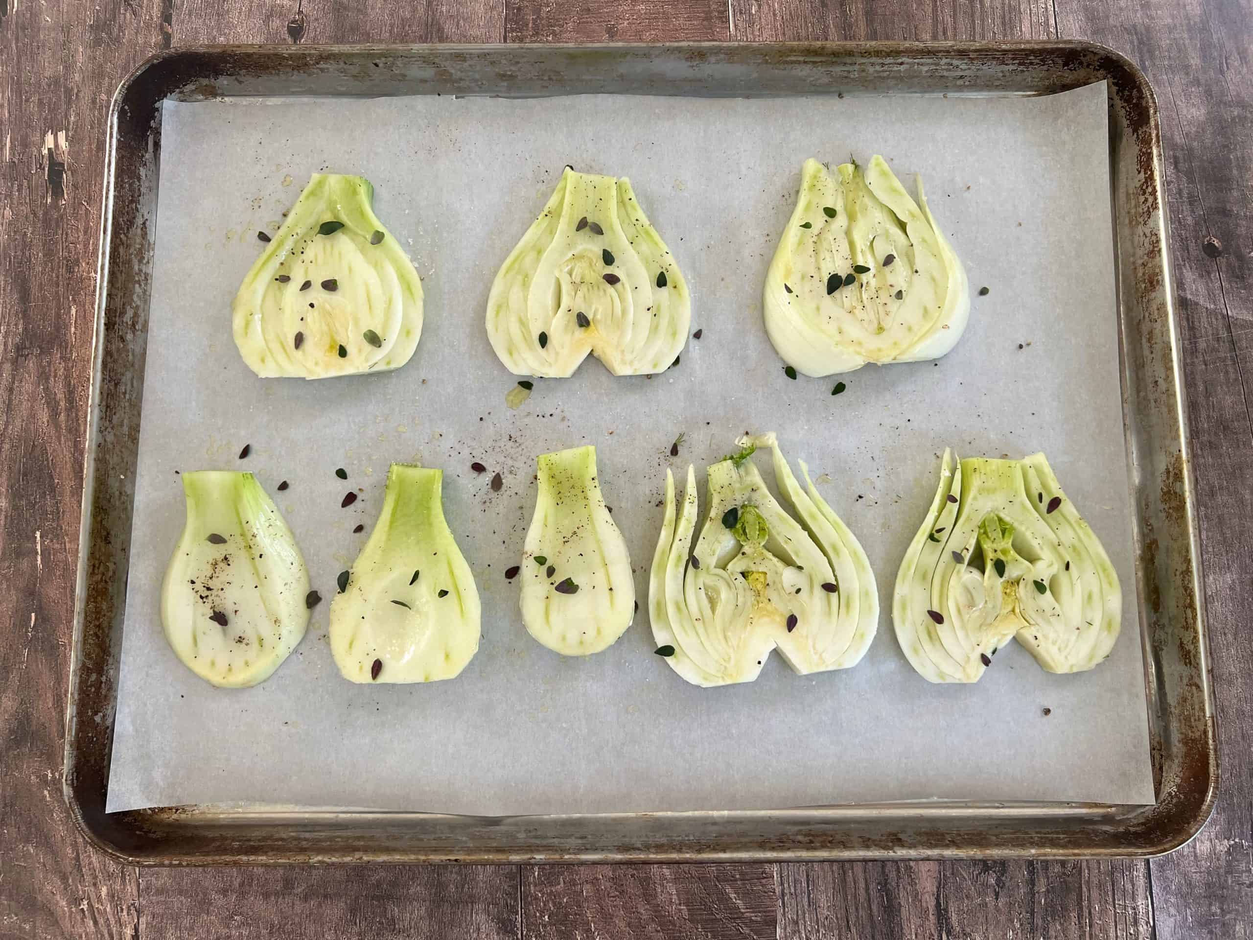 parchment lined baking sheet with thick slices of fennel drizzled with oil and sprinkled with thyme leaves