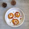 plate with 3 roasted sweet potato slices topped with goat cheese, pistachios, pomegranate seeds, orange zest and honey drizzle and two pine cones in the background