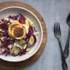 bowl of winter slaw made with fennel apple, cabbage and orange, topped with two slices of blood orange and fennel fronds. a fork and spoon resting next to the bowl