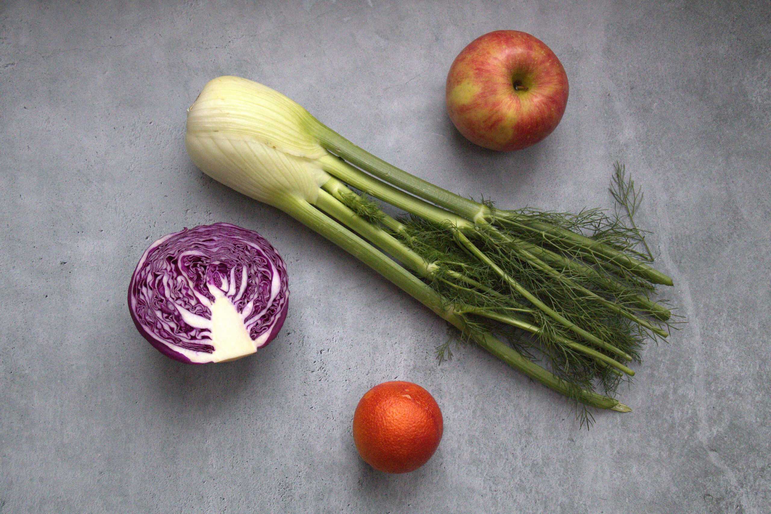 whole slaw ingredients, including an apple, fennel bulb, half a head of red cabbage and a blood orange