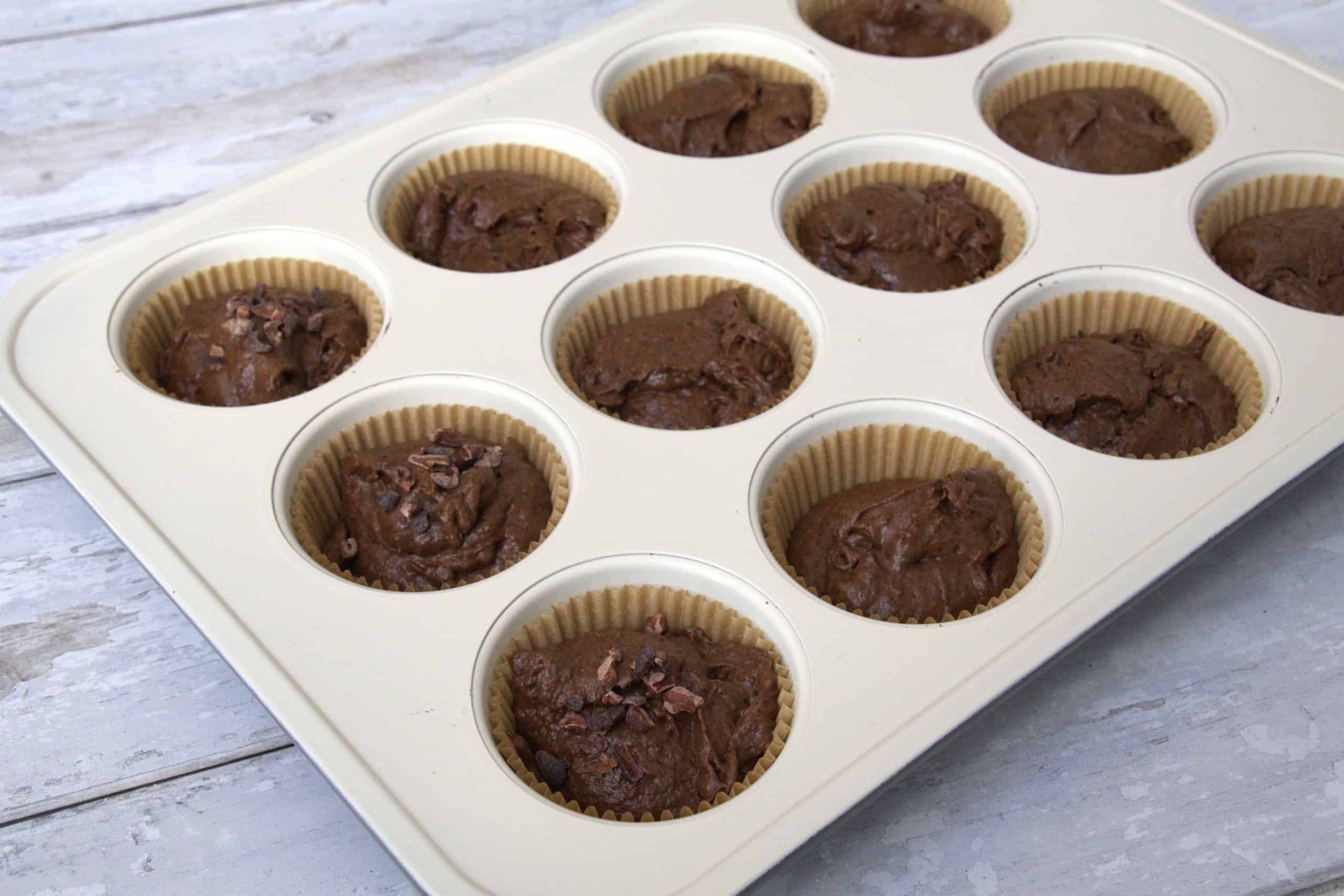 batter for spiced date chocolate muffins in muffin tins with some of the batter sprinkled with cacao nibs