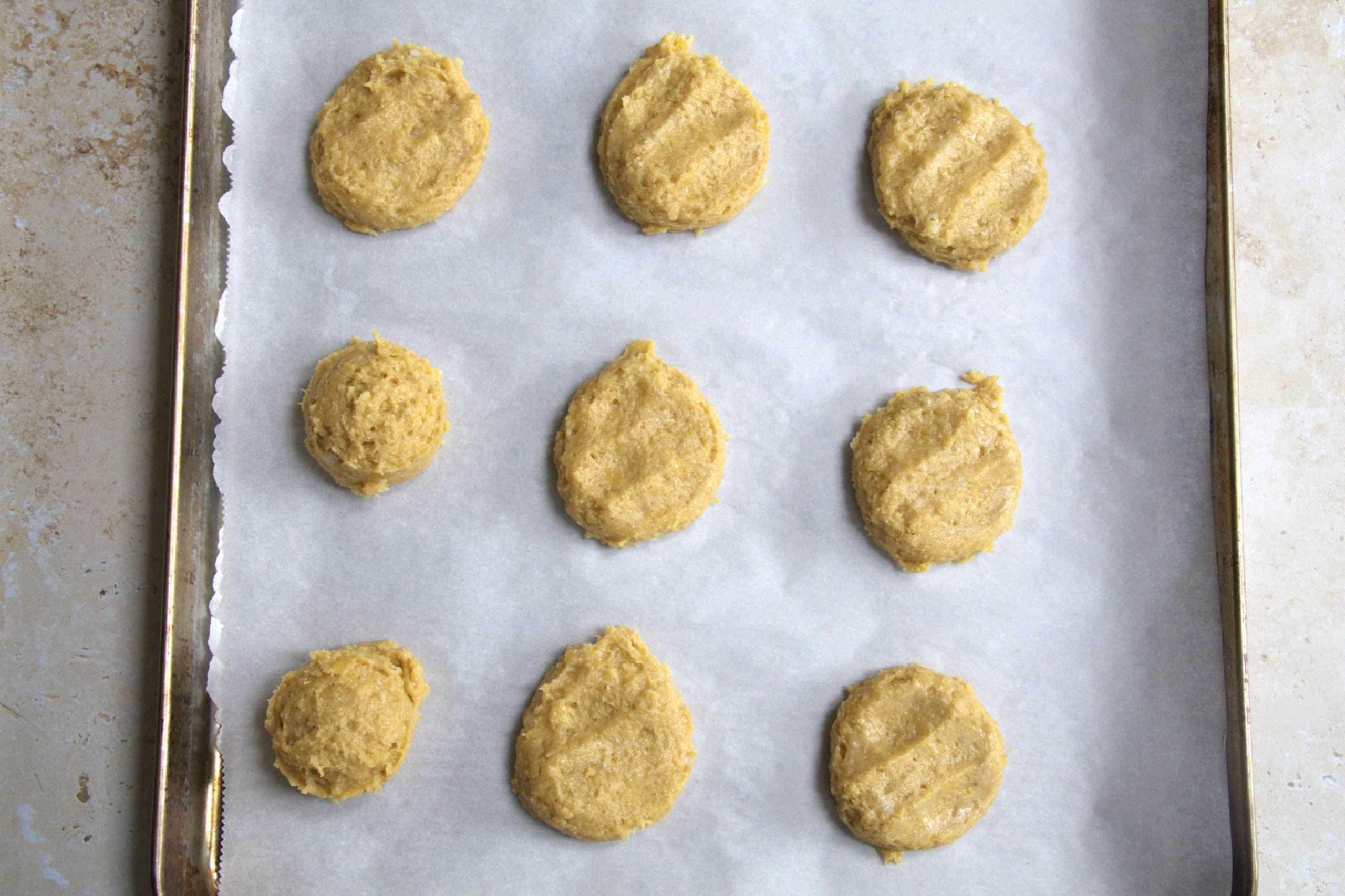 Tablespoon sized balls of cookie dough on a baking sheet - several of them have been lightly flattened