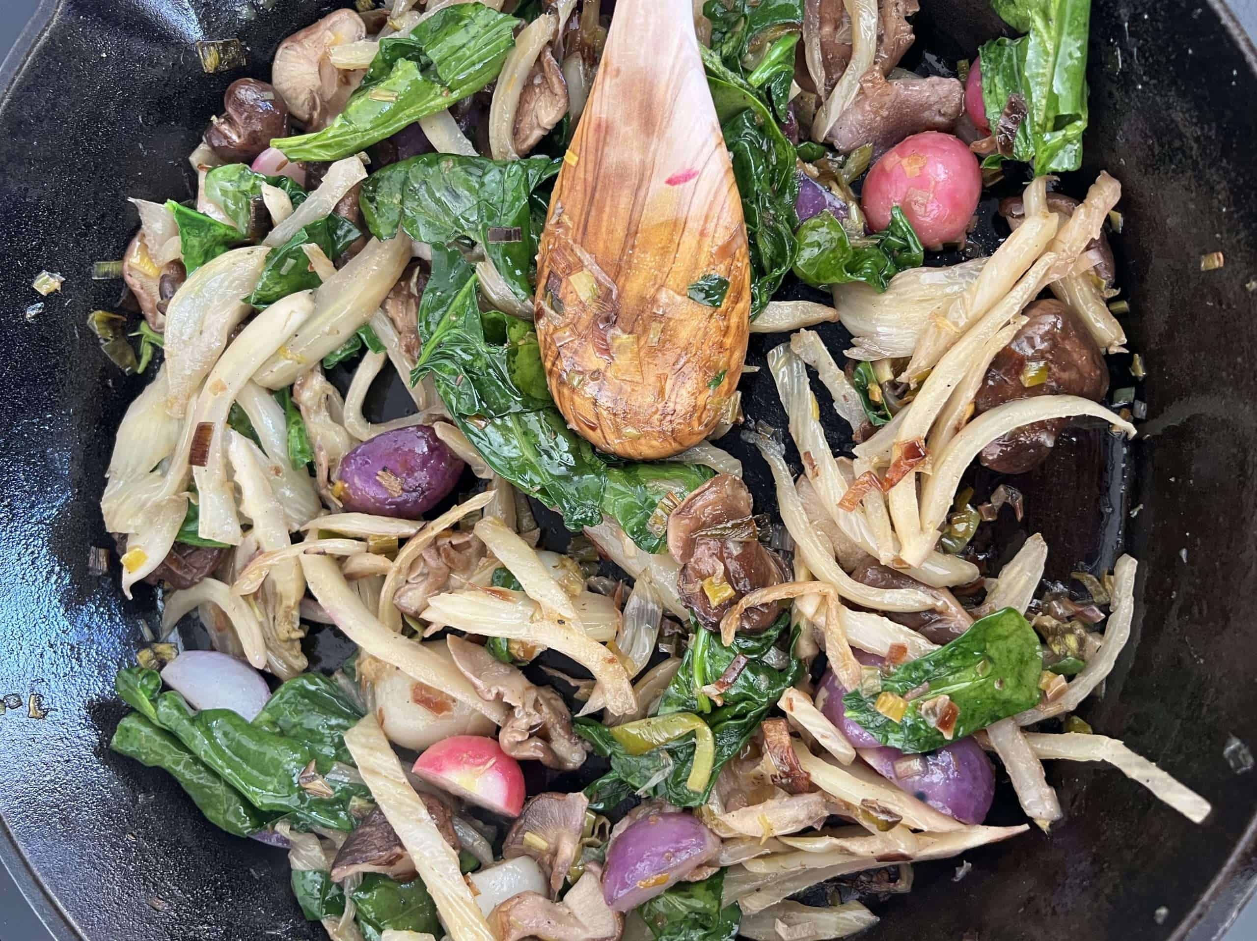 A medley of sauteed vegetables, including colorful radishes, sliced fennel, shiitake mushrooms, leeks and spinach