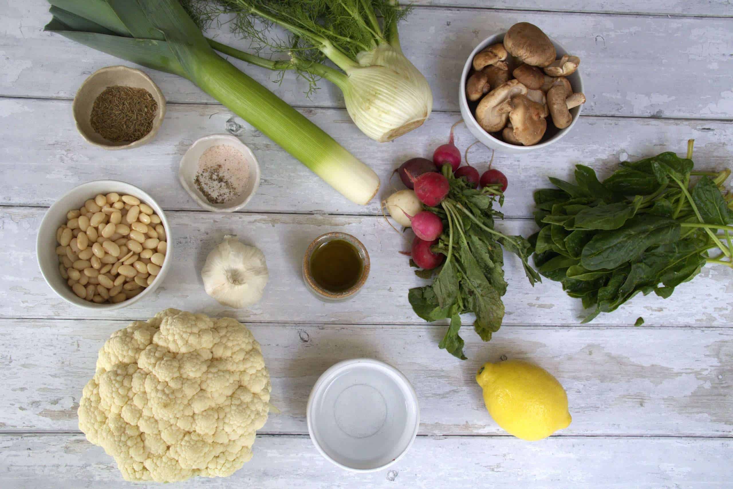 all ingredients for sauteed spring vegetables with white bean cauliflower purée displayed, including fennel, leek, radishes, shiitake mushrooms, spinach, white beans, cauliflower, garlic, lemon, cumin seeds and seasonings