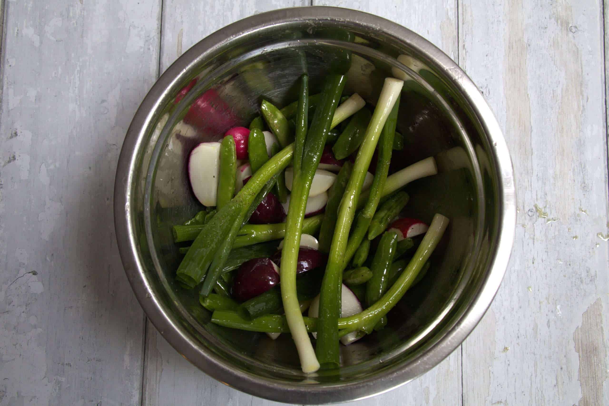 A bowl with scallions, radishes, and sugar snap peas all drizzled with extra virgin olive oil and sprinkled with fine sea salt and black pepper