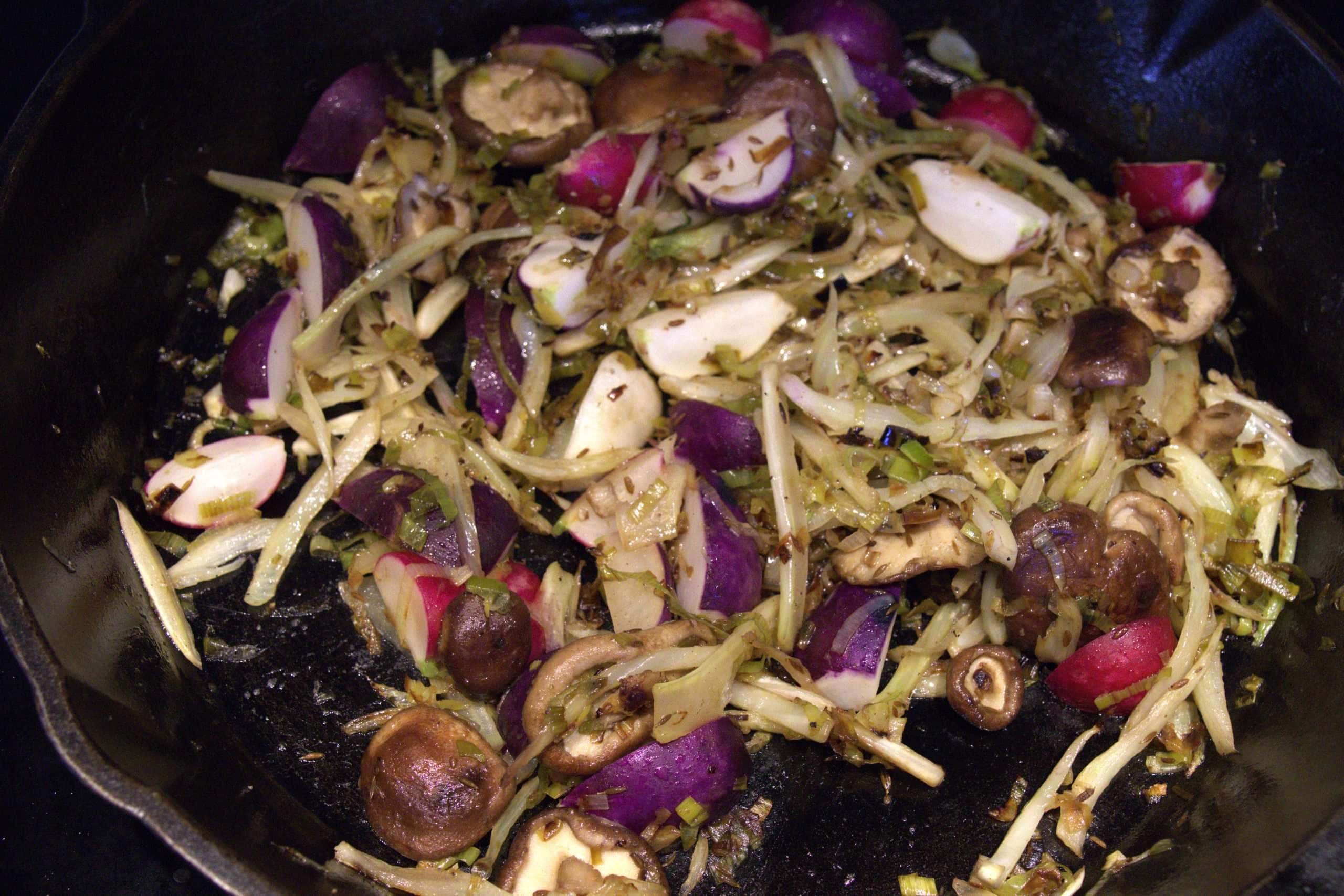 Thinly sliced fennel, leeks, shiitake mushrooms and radishes being sauteed in a pan