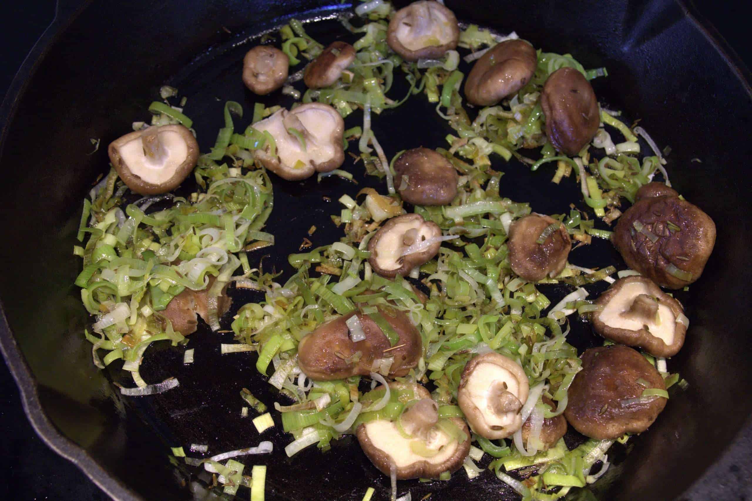 Leeks and shiitake mushrooms cooking in a cast iron pan
